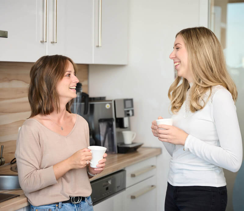 Zwei Mitarbeiterinnen der Steuerkanzlei Schweiger lachen gemeinsam in der Kaffeeküche